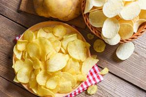 lanche de batatas fritas no prato, batatas fritas crocantes na mesa da cozinha e batatas cruas frescas em fundo de madeira - vista superior foto