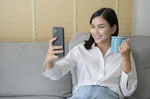 jovem mulher feliz relaxando e usando telefone inteligente em casa, mídia social e conceito de tecnologia. foto