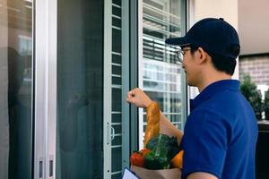 homem asiático segurando um pé de saco de comida batendo na porta da frente. foto