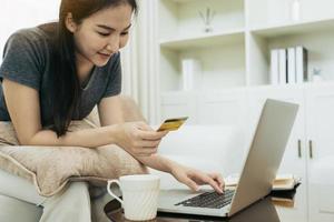 mulher asiática segurando um cartão de crédito para compras online enquanto está sentado no sofá durante as férias em casa. foto