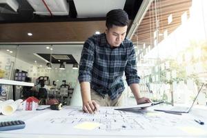 designer de interiores ou arquiteto revisando plantas e segurando o desenho a lápis na mesa do escritório em casa. foto