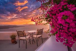 bela vista da caldeira e apreciando a paisagem romântica pôr do sol mar egeu, santorini. férias de viagem de casal, destino de lua de mel. romance com flores, mesa de duas cadeiras e vista para o mar. férias de luxo foto