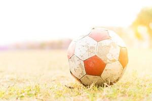 o velho futebol vermelho e branco no campo de grama com luz solar. foto