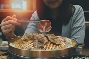 mulher asiática comendo comida yakiniku versão japonesa do churrasco coreano. carne crua em um prato e carne grelhada com molho. wagyu a5 carne japonesa considerada a melhor carne bovina do mundo foto