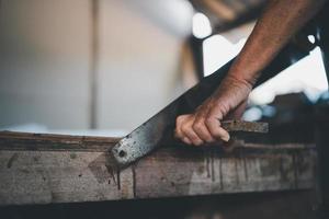 velho carpinteiro sênior usando serra trabalhando em artesanato de madeira na oficina para produzir material de construção ou móveis de madeira. foto