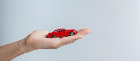mão de empresário segurando o brinquedo do carro vermelho. seguro de carro, garantia, aluguel, financeiro, novo e conceito de reparo foto