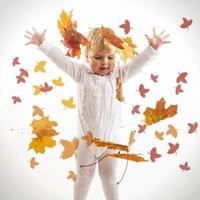 linda criança brincando com as folhas de outono