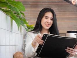 jovem empresária asiática linda sorrindo e posando enquanto está sentado em um café moderno. jovem mulher atraente sentada em um café interior e olhando feliz para a câmera. foto