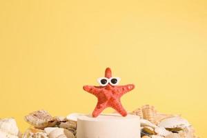 estrela do mar em óculos de sol em um pedestal entre conchas em um fundo amarelo. conceito criativo de verão foto