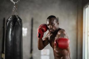 homem africano treinando no ginásio e punhos seus punhos de saco de boxe. homem esporte treinando na academia, fitness, boxe, sucesso, treino e poder foto