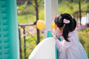 linda garota asiática joga na escola ou jardim de infância ou playground. atividade de verão saudável para crianças. menina asiática escalando ao ar livre no playground. criança brincando no playground ao ar livre. foto