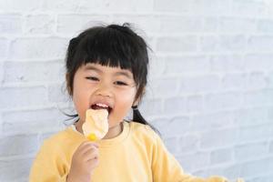 menina asiática comendo sorvete em fundo cinza. conceito de estilo de vida do bebê foto