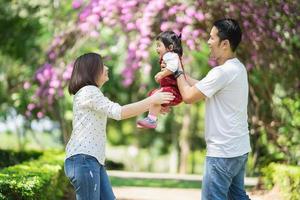 lindo retrato de família asiática sorrindo e feliz. pais jogando filha no jardim. conceito de família feliz. foto