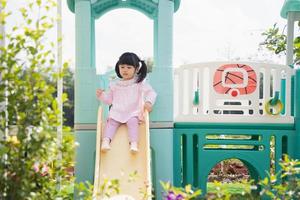 linda garota asiática joga na escola ou jardim de infância ou playground. atividade de verão saudável para crianças. menina asiática escalando ao ar livre no playground. criança brincando no playground ao ar livre. foto