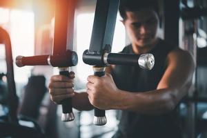 homem esporte usando exercício de máquina esportiva na academia. fisiculturismo asiático para treinamento muscular. conceito de ginásio de saúde esportiva foto