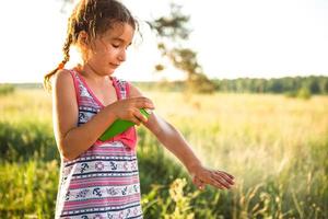 menina pulveriza spray de mosquito na pele na natureza que morde as mãos e os pés. proteção contra picadas de insetos, repelente seguro para crianças. recreação ao ar livre, contra alergias. horário de verão foto