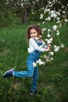 uma menina bonitinha de 5 anos em um pomar de maçãs brancas florescendo na primavera. primavera, pomar, floração, alergia, fragrância primaveril, ternura, cuidado com a natureza. retrato foto