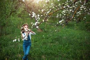 uma menina bonitinha de 5 anos em um pomar de maçãs brancas florescendo na primavera. primavera, pomar, floração, alergia, fragrância primaveril, ternura, cuidado com a natureza. retrato foto