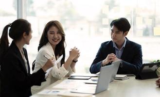 grupo de jovens empresários trabalhando e se comunicando enquanto estão sentados na mesa do escritório junto com colegas sentados em segundo plano foto