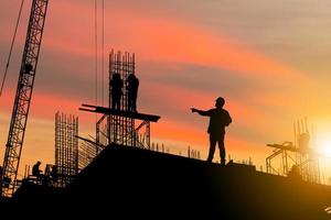 silhueta de engenheiro e trabalhador no canteiro de obras, canteiro de obras ao pôr do sol à noite foto