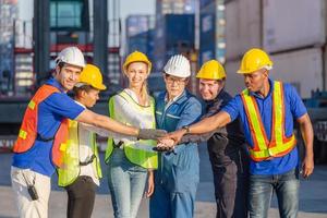 conceito de trabalho em equipe de sucesso e felicidade, grupo de empresários, equipe de engenheiros e trabalhadores juntando as mãos com fundo de contêineres de carga turva foto