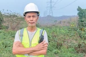 retrato de um engenheiro sênior em pé com os braços cruzados em um poste de alta tensão. foto