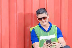 homem engenheiro em óculos de sol usa telefone celular, trabalhador industrial usando smartphone móvel na carga de contêineres da indústria foto