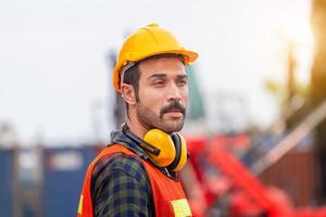 retrato de engenheiro homem de capacete e colete de segurança, trabalhador com fones de ouvido protetores no canteiro de obras foto