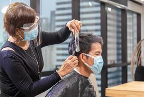 cabeleireiro e cliente usando máscara protetora devido à pandemia de coronavírus, barbeiro usando tesoura e pente, jovem cortando o cabelo pelo cabeleireiro, novos conceitos normais
