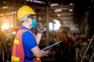 engenheiro sob inspeção e verificando o processo de produção na estação de fábrica segurando a chave de fenda usando máscara de segurança para proteger contra poluição e vírus na fábrica. foto