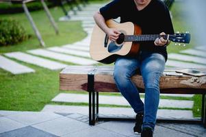 foto de um guitarrista, um jovem tocando violão enquanto está sentado em um jardim natural, conceito de música