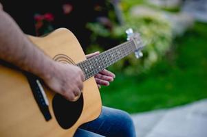 foto de um guitarrista, um jovem tocando violão enquanto está sentado em um jardim natural, conceito de música