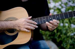 foto de um guitarrista, um jovem tocando violão enquanto está sentado em um jardim natural, conceito de música