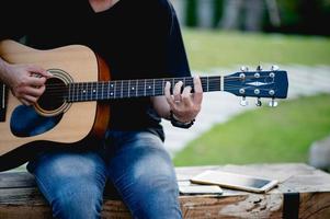 foto de um guitarrista, um jovem tocando violão enquanto está sentado em um jardim natural, conceito de música