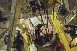 vista superior masculina subir as escadas para o tanque área química inoxidável espaço confinado salvar vidas com corda de resgate foto