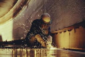 trabalhador do sexo masculino cortando faísca na placa de aço do fundo do tanque com flash de luz de corte close-up usar luvas de proteção e máscara