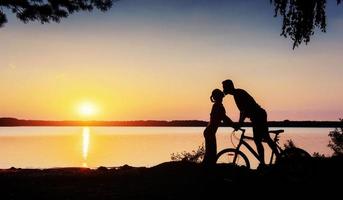 casal de bicicleta ao pôr do sol à beira do lago foto