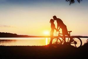 casal de bicicleta ao pôr do sol à beira do lago foto