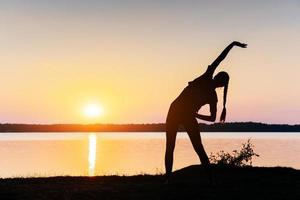 menina ao pôr do sol à beira do lago foto