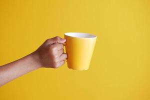 close-up da mão do homem segurando a caneca isolada em amarelo foto