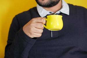 mão de jovem segurando uma caneca de café de cor amarela foto