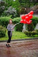 retrato de uma linda dama de honra linda em roupas casuais, segurando balões vermelhos em forma de coração no parque na despedida de solteira. foto