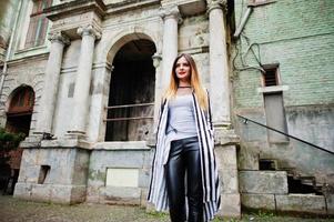 mulher elegante olhar com paletó listrado preto e branco, calça de couro, posando na rua velha. conceito de menina da moda. foto