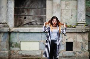 mulher elegante olhar com paletó listrado preto e branco, calça de couro, posando na rua velha. conceito de menina da moda. foto