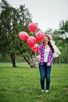retrato de menina morena na camisa quadriculada, jeans e véu com muitos balões vermelhos na festa de despedida.