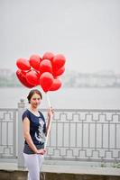 retrato de uma linda linda dama de honra vestida casualmente segurando balões vermelhos em forma de coração ao lado do lago na despedida de solteira.