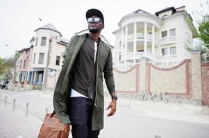 retrato de andar homem afro-americano elegante usar óculos escuros e boné com bolsa ao ar livre. homem negro da moda de rua. foto