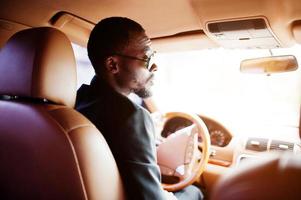 elegante homem negro sentado ao volante de um carro de luxo. rico empresário americano africano. foto