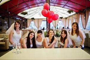 grupo de seis meninas sentadas à mesa na despedida de solteira, com balões. foto