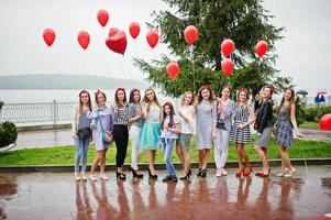 onze damas de honra incrivelmente bonitas com noiva deslumbrante posando com balões vermelhos em forma de coração na calçada contra o lago ao fundo.